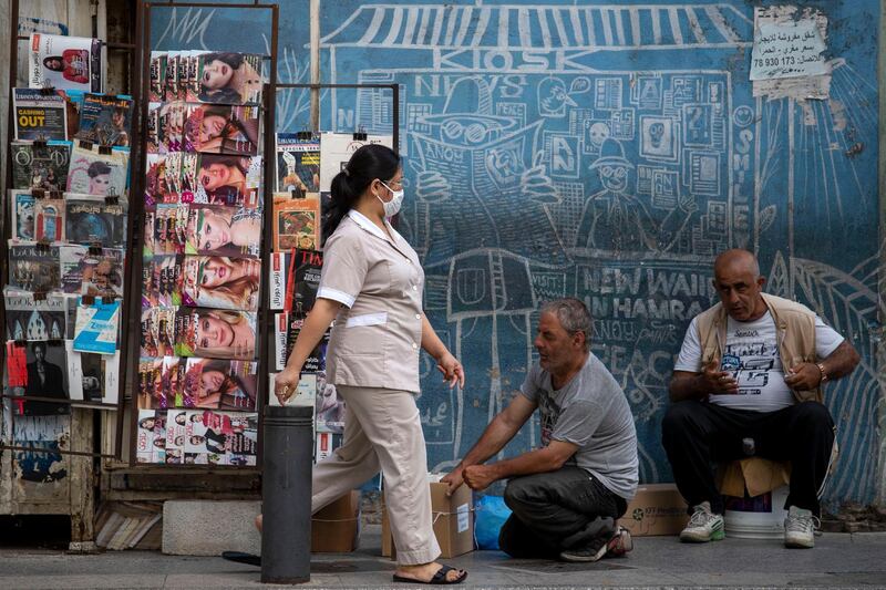 A maid from the Philippines wears a mask to help stop the spread of the new coronavirus as she walks in front of a newspaper kiosk in central Beirut's commercial Hamra Street, in Beirut, Lebanon. AP Photo