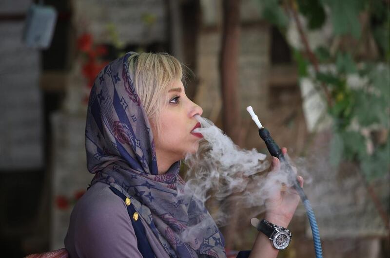 A woman smokes a hookah while visiting a poetry calligraphy workshop in Shiraz.