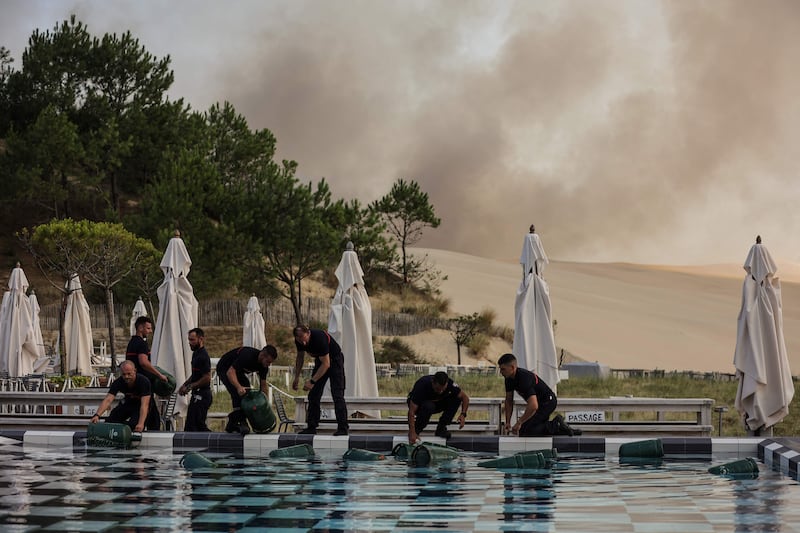 Firefighters put gas containers in the swimming pool of the 5 star hotel La Corniche in the town of Pilat sur Merle, in south-west France, as smoke from a fire is seen in background.  AFP