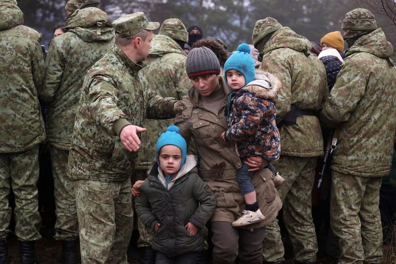 A group of migrants waits alongside Belarusian military personnel as humanitarian aid is distributed. AFP