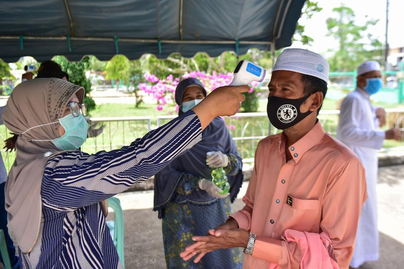 A public health officer checks the temperature of a Muslim man as he arrives to attend Friday prayers at a mosque in the southern Thai province of Narathiwat as restrictions aimed at curbing the spread of the COVID-19 novel coronavirus are slowly eased.   AFP