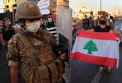 A Lebanese army soldier passes in front of an anti-government protester holding a national flag and blocking a main highway that links Beirut with north Lebanon during a protest against rising prices and worsening economic and financial conditions, in Zalka, north of Beirut, Lebanon, Monday, Oct. 5, 2020. Lebanon is passing through its worst economic and financial crisis in decades made worse by the coronavirus pandemic. (AP Photo/Hussein Malla)