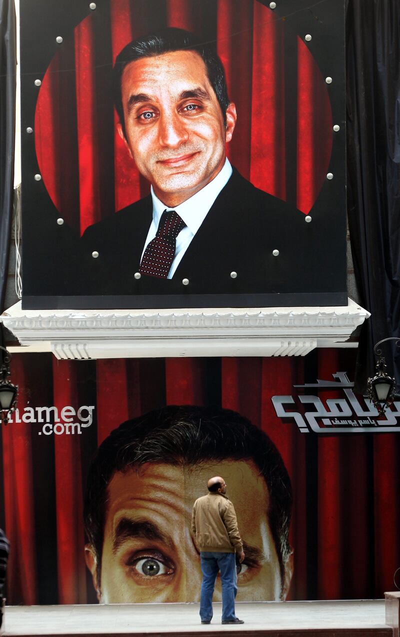 epa03522301 An Egyptian man stands in front of banners depicting Egyptian satirical TV show host Bassem Youssef in front of a theater in Cairo, Egypt, 02 January 2013.  Egyptian prosecutors on 01 January began investigating Youssef for allegedly defaming President Mohamed Morsi on his program. Youssef has been satirizing speeches by Islamists in his recent episodes, broadcast on a private Egyptian Satellite channel. Youssef is known as "Egypt's Jon Stewart" - a reference to the US political satirist who hosts Comedy Central's Daily Show.  EPA/KHALED ELFIQI *** Local Caption ***  03522301.jpg