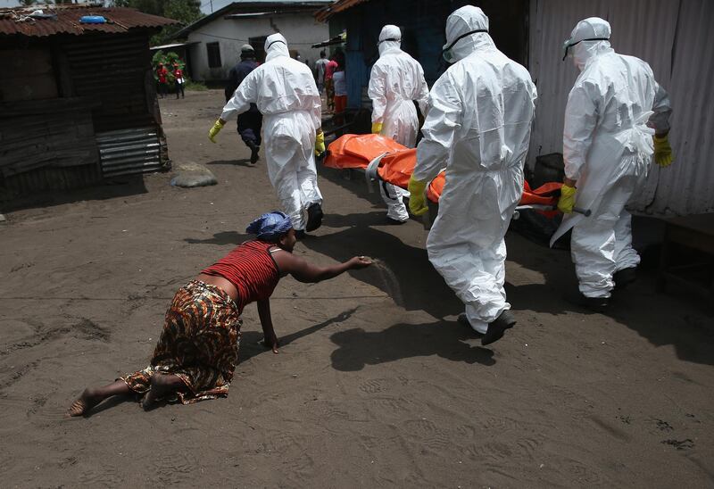 MONROVIA, LIBERIA - OCTOBER 10:  A woman throws a handful of soil towards the body of her sister as Ebola burial team members take her sister Mekie Nagbe, 28, for cremation on October 10, 2014 in Monrovia, Liberia. Nagbe, a market vendor, collapsed and died outside her home earlier in the morning while leaving to walk to a treatment center, according to her relatives. The burial of loved ones is important in Liberian culture, making the removal of infected bodies for cremation all the more traumatic for surviving family members. The World Health Organization says the Ebola epidemic has now killed more than 4,000 people in West Africa. (Photo by John Moore/Getty Images)