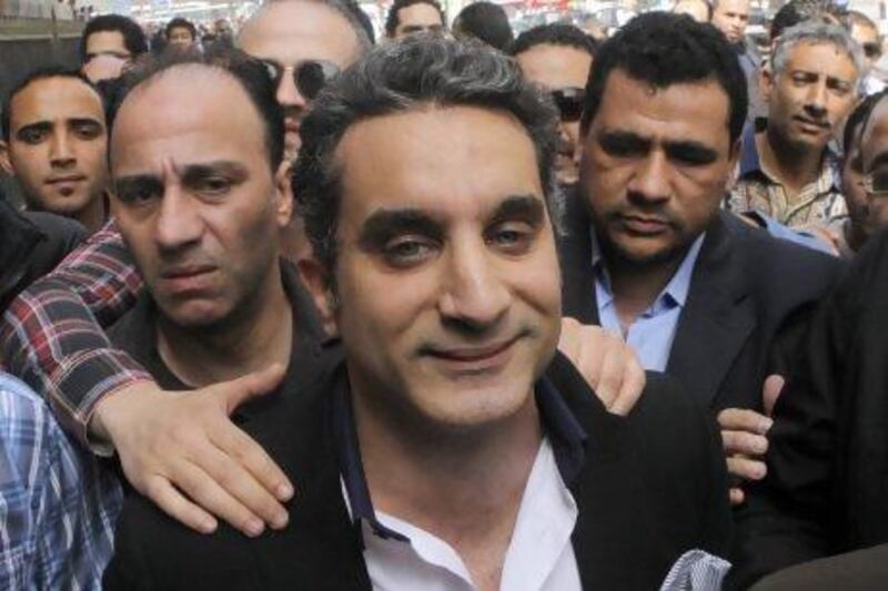 A bodyguard secures popular Egyptian television satirist Bassem Youssef, who has come to be known as Egypt's Jon Stewart, as he enters Egypt's state prosecutors office to face accusations of insulting Islam and the country's Islamist leader.