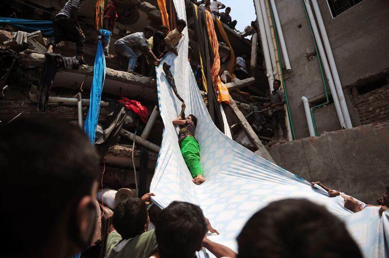 Bangladeshi garment workers help evacuate a survivor using lengths of textile as a slide to evacuate from the rubble after an eight-storey building collapsed in Savar, on the outskirts of Dhaka, on April 24, 2013. At least 15 people were killed and many more feared dead when an eight-storey building housing a market and garment factory collapsed in Bangladesh on Wednesday, officials said.  AFP PHOTO/Munir uz ZAMAN
 *** Local Caption ***  978783-01-08.jpg