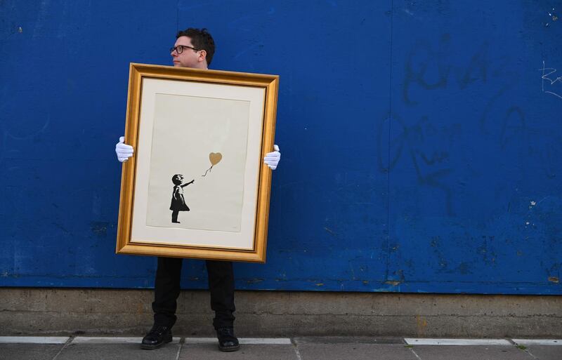 An employee of auction house Christie's poses with 'Girl with Balloon' (Gold) by British street artist Banksy at the Southbank centre, in London on August 30, 2019. RESTRICTED TO EDITORIAL USE - MANDATORY MENTION OF THE ARTIST UPON PUBLICATION - TO ILLUSTRATE THE EVENT AS SPECIFIED IN THE CAPTION
 / AFP / DANIEL LEAL-OLIVAS / RESTRICTED TO EDITORIAL USE - MANDATORY MENTION OF THE ARTIST UPON PUBLICATION - TO ILLUSTRATE THE EVENT AS SPECIFIED IN THE CAPTION
