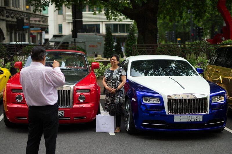 A woman poses for a photograph between a Saudi Arabian-registered and a Kuwaiti-registered Rolls-Royce. Carl Court / Getty Images