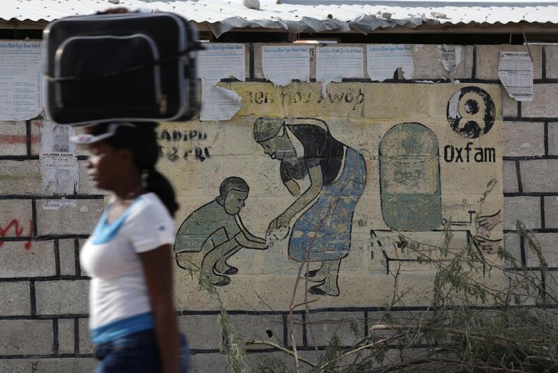 A woman walks carrying a suitcase on her head next to an Oxfam sign in Corail, a camp for displaced people of the 2010 earthquake, on the outskirts of Port-au-Prince, Haiti, February 13, 2018. REUTERS/Andres Martinez Casares