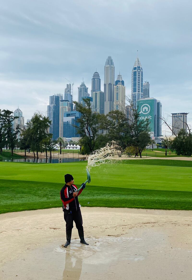 A member of staff attempts to clear standing water from a bunker beside the first fairway. Paul Radley / The National