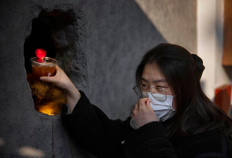 epa08861368 A woman, wearing a mask for protection, receives her order at Hinichijou, also known as 'Hole in the wall' cafe in Shanghai, China, 04 December 2020. 'Hole in the wall' cafe introduced a new way of ordering and consuming coffee among Shanghai citizens. Costumers scan a code for ordering and payment and several minutes later their coffee appears in artificial bear claw through a hole in the wall. Sometimes the claw delivers a rose with the coffee to female customers. Hinichijou provides employment to three baristas with disabilities, some of whom prefer to avoid contact with customers due to their disibility. During the COVID-19 pandemic in China, the cafe provides a safe environment for the baristas to continue working. The cafe also provides free coffee for disabled costumers. Located in Shanghai’s Yongkang Road, the cafe somtimes attracts so many people they block the street, due to its innovative way of doing business.  EPA/ALEX PLAVEVSKI