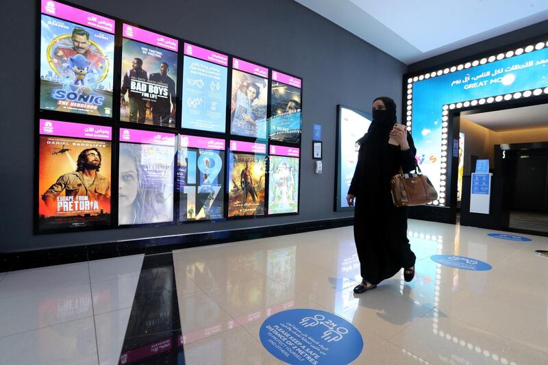 A Saudi woman wearing a protective mask walks past the movie screen board at VOX Cinema in Riyadh Park Mall. Reuters