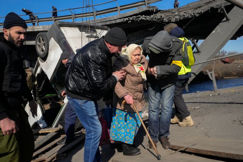 Volunteers pass an improvised path under a destroyed bridge as they help an elderly resident in Irpin, north-west Kyiv. AP Photo