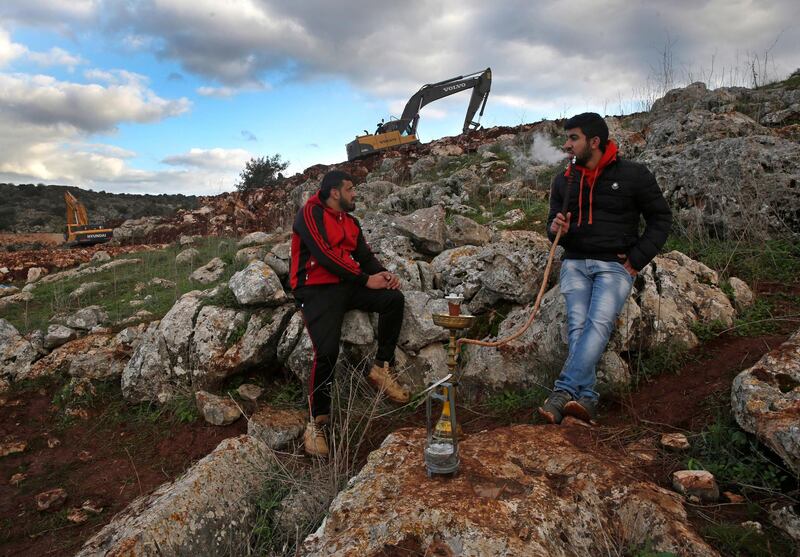 Lebanese villagers smoke shisha as Israeli soldiers work near the border. AP Photo