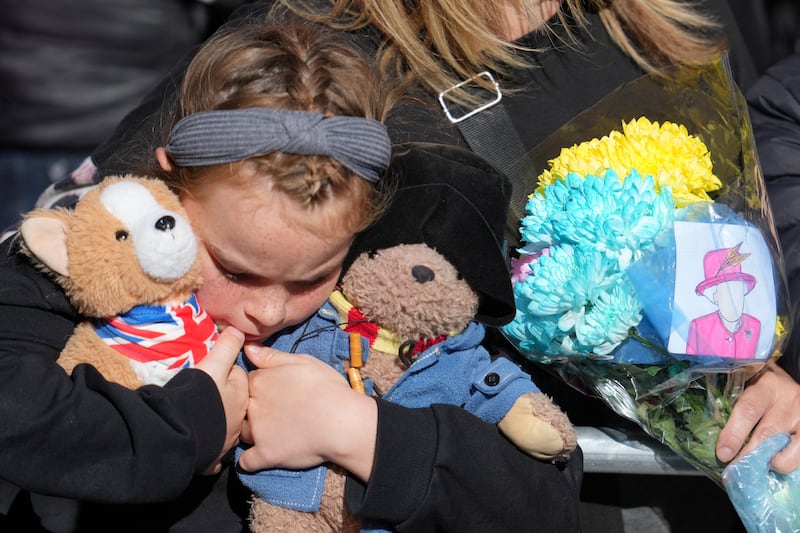 A young girl holds a Paddington bear and a Corgi dog stuffed toys while waiting to watch the procession. Getty