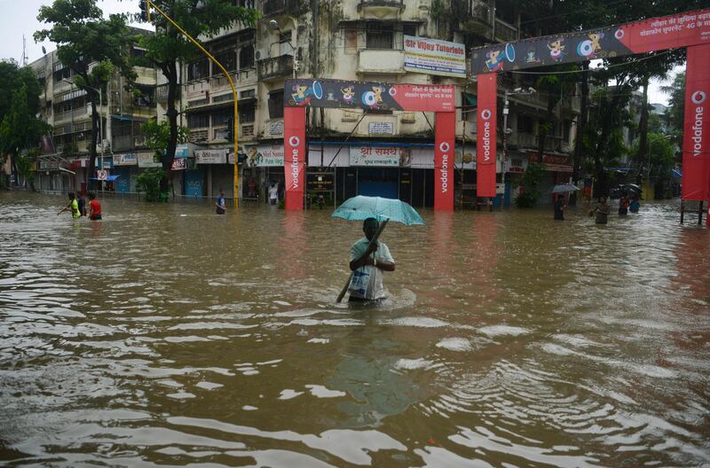 An Indian man holding an umbrella wades through a flooded street during heavy rain showers in Mumbai.  Punit Paranjpe / AFP