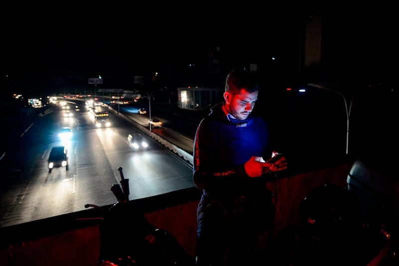 A man checks his mobile phone in Caracas on July 22, 2019 while the capital and other parts of Venezuela are being hit by a massive power cut. The lights went out in most of Caracas while people in other parts of the country took to social media to report the power had gone out there too. The state-owned power company CORPOELEC only reported a breakdown affecting sectors of Caracas. / AFP / Matias Delacroix
