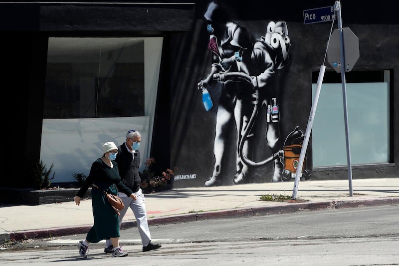 People wearing masks walk past a mural depicting the coronavirus in Los Angeles. AP Photo