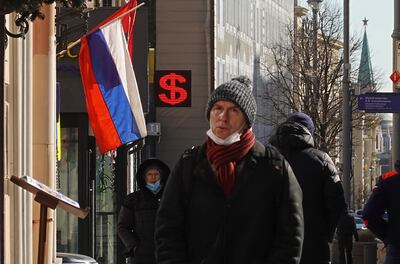 People walk in front of an electronic panel displaying a US dollar sign at an exchange office in Moscow. Emerging market currencies are likely to remain under pressure as the greenback's strength increases the cost of servicing their debts. EPA 