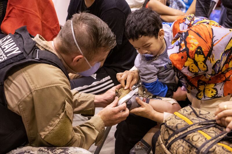 A sailor helps a young child try on a new pair of shoes. Photo: US Department of Defence