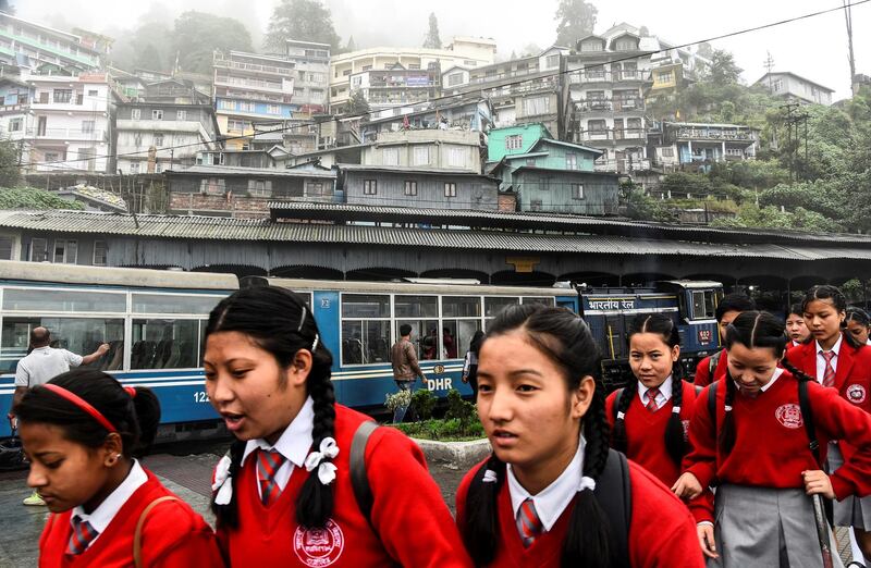 School children walk past a parked Darjeeling Himalayan Railway train at a station in Darjeeling.