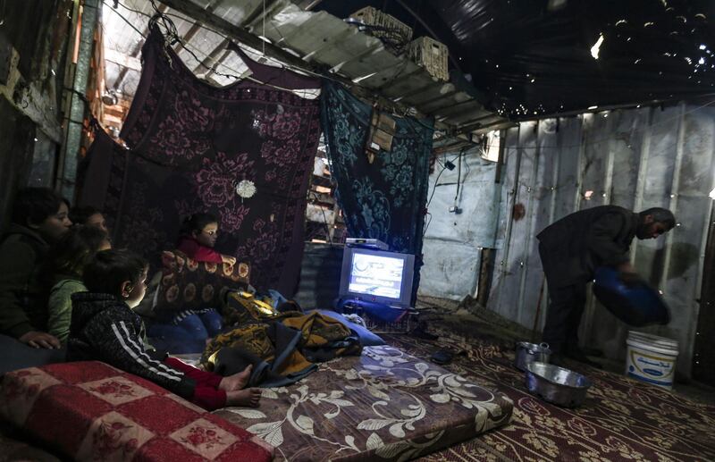 A Palestinian man removes a basin filled with water from a leaking roof inside his family tent made of tin and nylon sheets, as children huddle in a corner to watch television, on a rainy day in al-Amal (hope in Arabic) neighbourhood of Beit Lahia in the northern Gaza Strip.  AFP