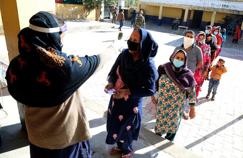 An Indian polling official checks a voter's temperature at a polling station during the first phase of the District Development Council (DDC) elections at Garkhal village near India-Pakistan international border in Akhnoor, India.   EPA