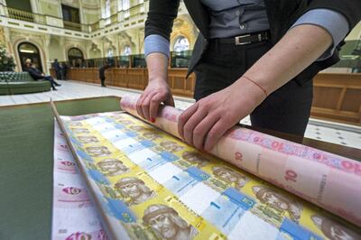 A bank worker rolls up uncut sheets of ten and one hryvnia banknotes after arranging for a photograph at the headquarters of the National Bank of Ukraine in Kiev, Ukraine, on Tuesday, March 22, 2016.  Ukraine's political gridlock, already holding up billions of dollars in aid, is also threatening financial stability and postponing monetary easing, according to the nations central bank governor. Photographer: Vincent Mundy/Bloomberg
