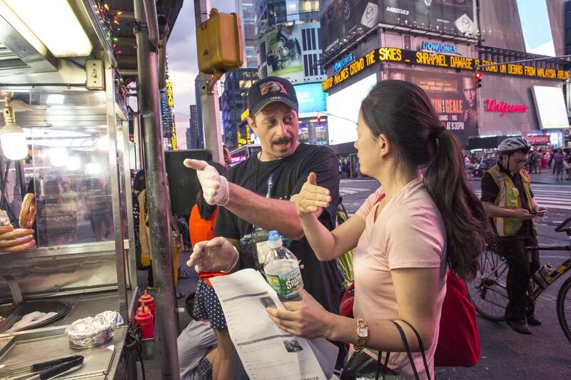Mohammed Omar, originally from Egypt, gives a customer directions at his halal food cart during Ramadan on the corner of 42nd Street and Broadway in Times Square in New York. Michael Kirby Smith for The National 
