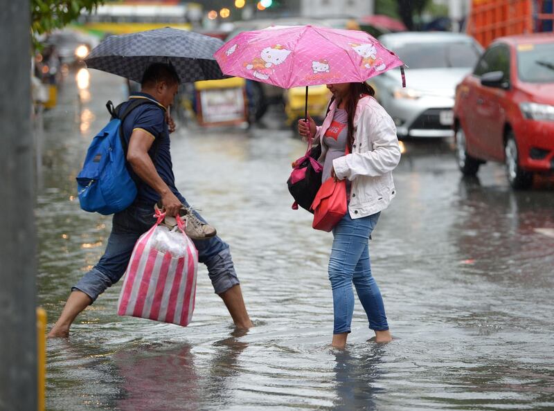 People cross a flooded street in Manila. AFP