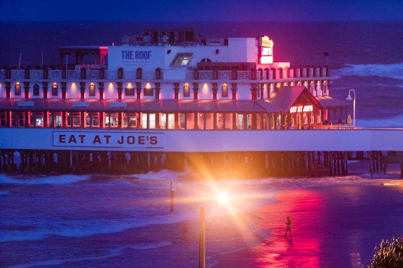 A beachgoer walks through rising surf next to the Main Street Pier at dusk in Daytona Beach. EPA