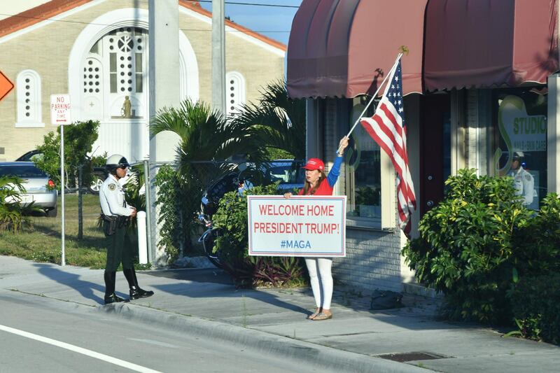 A supporter holds a signs and a flag cheering for Donald Trump after his arrival in West Palm Beach, Florida on April 18, 2019. / AFP / Nicholas Kamm