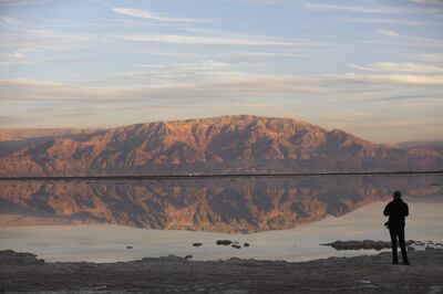 TOPSHOT - A Picture taken on January 3, 2018 shows a tourist walking next to evaporation ponds in the southern part of the Dead Sea, where both sodium chloride and potassium salts are produced, near the Neve Zohar resort, as Jordan's mountains are seen in the back. / AFP PHOTO / MENAHEM KAHANA