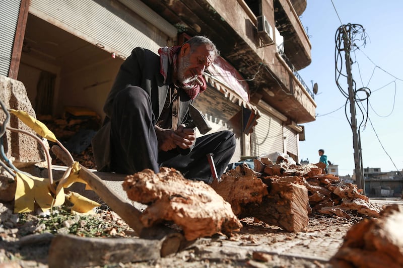 An elderly Syrian uses a hammer and chisel to chop firewood in the town of Douma in the rebel-held Eastern Ghouta region, east of the capital Damascus on November 11, 2017. / AFP PHOTO / ABDULMONAM EASSA