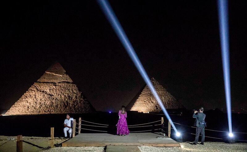 A woman poses for a picture as a policeman watches while sitting by along a promontory looking onto the the Great Pyramid of Khufu (Cheops) and the Pyramid of Khafre (Chephren) at the Giza Pyramids necropolis on the southwestern outskirts of the Egyptian capital Cairo during an official ceremony launching the trial operations of the site's first environmentally-friendly electric bus (foreground) and restaurant as part of a wider development plan at the necropolis.  AFP