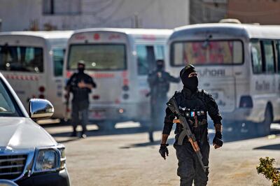 Members of Kurdish security forces stand next to buses carrying the families of ISIS fighters in Syria's Hasakah province. AFP