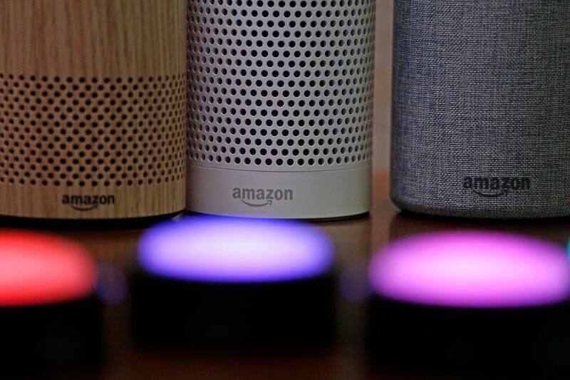 FILE - In this Sept. 27, 2017, file photo, Amazon Echo and Echo Plus devices, behind, sit near illuminated Echo Button devices during an event announcing several new Amazon products by the company in Seattle.  Amazon is expanding its home-security business by buying Ring, the maker of Wi-Fi-connected doorbells. The deal comes months after the online retailer started selling its own Wi-Fi-connected indoor security cameras, which work with its voice-assistant Alexa. (AP Photo/Elaine Thompson, File)