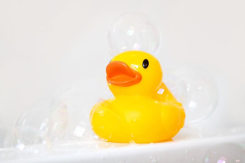 Yellow rubber ducky bath toy on edge of bathtub with bubbles all around. Getty Images