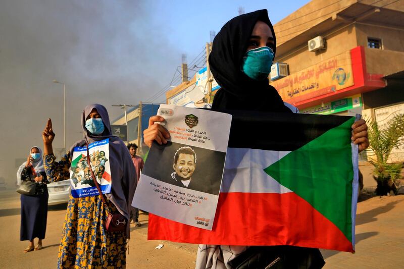 A mask-clad Sudanese woman holds a national flag along with a poster depicting the face of a slain protester, as demonstrators mark the first anniversary of a raid on an anti-government sit-in, in the Riyadh district in the east of the capital Khartoum. AFP