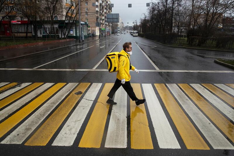 In this photo taken on Thursday, April 16, 2020, Russian businessman Sergey Nochovnyy wearing a face mask to protect against coronavirus crosses a road, on his way to pick up a food order to deliver, in Moscow, Russia. A Russian businessman has become a delivery man amid the nationâ€™s partial economic shutdown due to the coronavirus. Nochovnyy said that he hasnâ€™t lost his business and made the move to â€œchange an angleâ€ and avoid being locked at home amid the epidemic. (AP Photo/Pavel Golovkin)