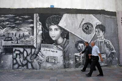Palestinian men walk in front a mural painted on a wall of the headquarters of the United Nations Relief and Works Agency (UNRWA) in Gaza City on October 2, 2018, closed in protest against job cuts announced by the UNRWA.  Earlier this year, the United States, by far the biggest contributor to the agency, announced it was halting its funding to the organisation, which it labelled "irredeemably flawed".
 / AFP / SAID KHATIB
