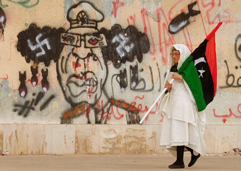 A Libyan woman holding a flag as she walks past a caricature of Muammar Qaddafi near the court house in Benghazi. Reuters