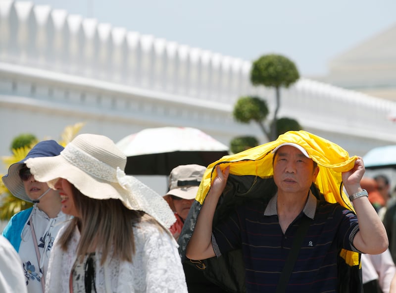 Chinese tourists shield themselves from sunlight during a hot day outside the Grand Palace in Bangkok on Monday.  The Thai Meteorological Department has advised the public to avoid prolonged outdoor activities. EPA