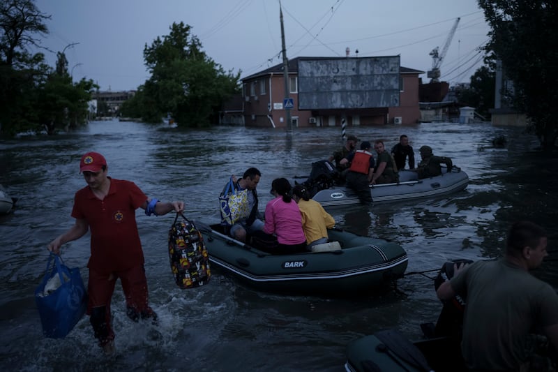 An emergency worker carries the belongings of residents being evacuated from a flooded neighborhood. AP