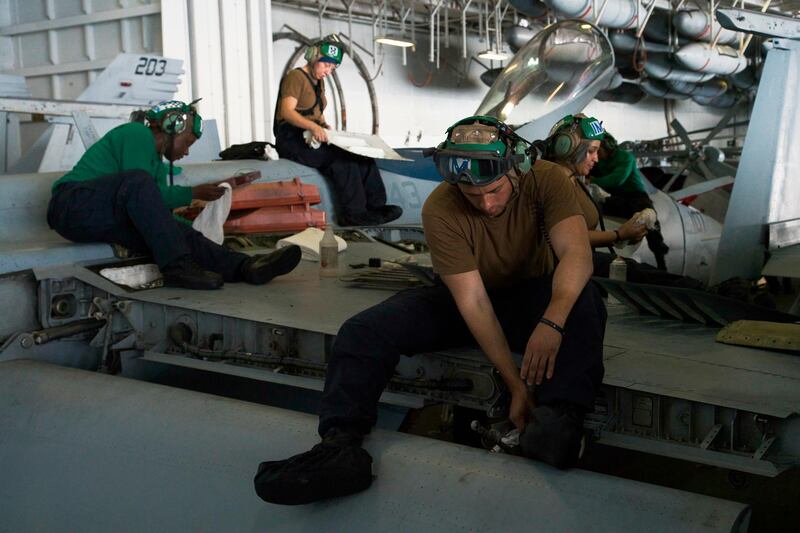 Sailors, including Petty Officer 2nd Class Phillip LeBron, 22, of Florida, centre, work atop an F/A-18 fighter jet in the hanger of the USS Abraham Lincoln aircraft carrier in the Arabian Sea on Monday, . AP