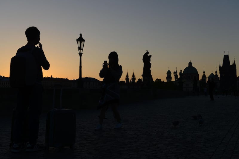 A tourist takes pictures as statues of the Charles Bridge silhouette against the sky during sunrise in Prague, Czech Republic. Michal Cizek / AFP