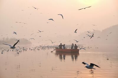 TOPSHOT - Indian women take pictures on a boat as migratory birds fly overhead on the Yamuna River on a morning of heavy air pollution in New Delhi on November 20, 2018. Smog levels spike during winter in Delhi, when air quality often eclipses the World Health Organization's safe levels. Cooler air traps pollutants -- such as from vehicles, building sites and farmers burning crops in regions outside the Indian capital -- close to the ground. / AFP / Noemi Cassanelli
