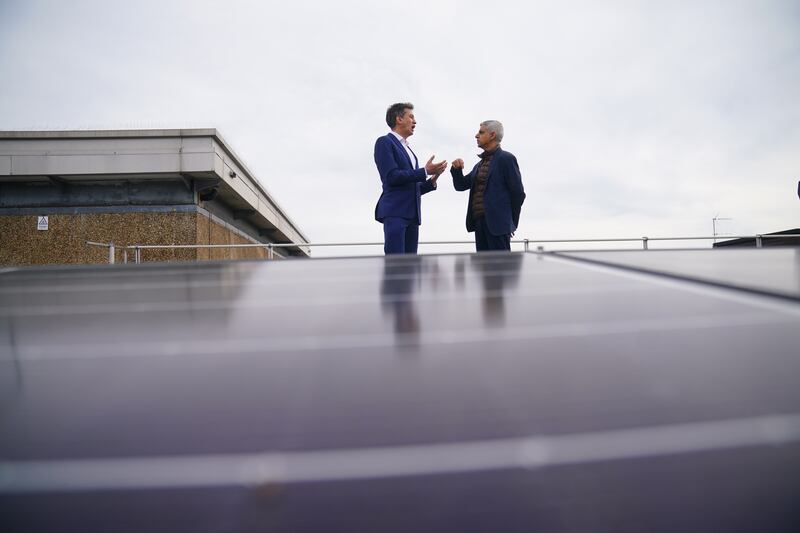 Mr Khan and shadow energy secretary Ed Miliband stand behind solar panels on the roof of Stoke Newington School in north London, during a visit to announce a new climate action plan for the city. PA