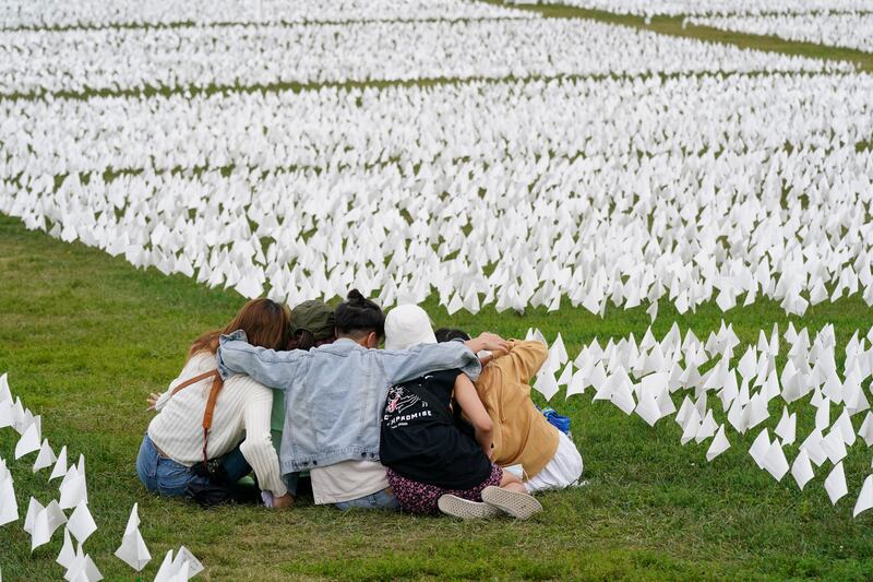 FILE - In this Sept.  21, 2021, file photo, visitors sit among white flags that are part of artist Suzanne Brennan Firstenberg's "In America: Remember," a temporary art installation to commemorate Americans who have died of COVID-19, on the National Mall in Washington.  Firstenberg was struck by how strangers connected in their grief at the installation, which ended Oct.  3.  (AP Photo / Patrick Semansky, File)