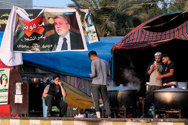 Volunteers prepare free food next to a poster of Iraq's Prime Minister-designate Mohammed Allawi with Arabic that reads, "Rejected by the people" during ongoing anti-government protests in Tahrir Square, Baghdad, Iraq, Thursday, Feb. 20, 2020. AP